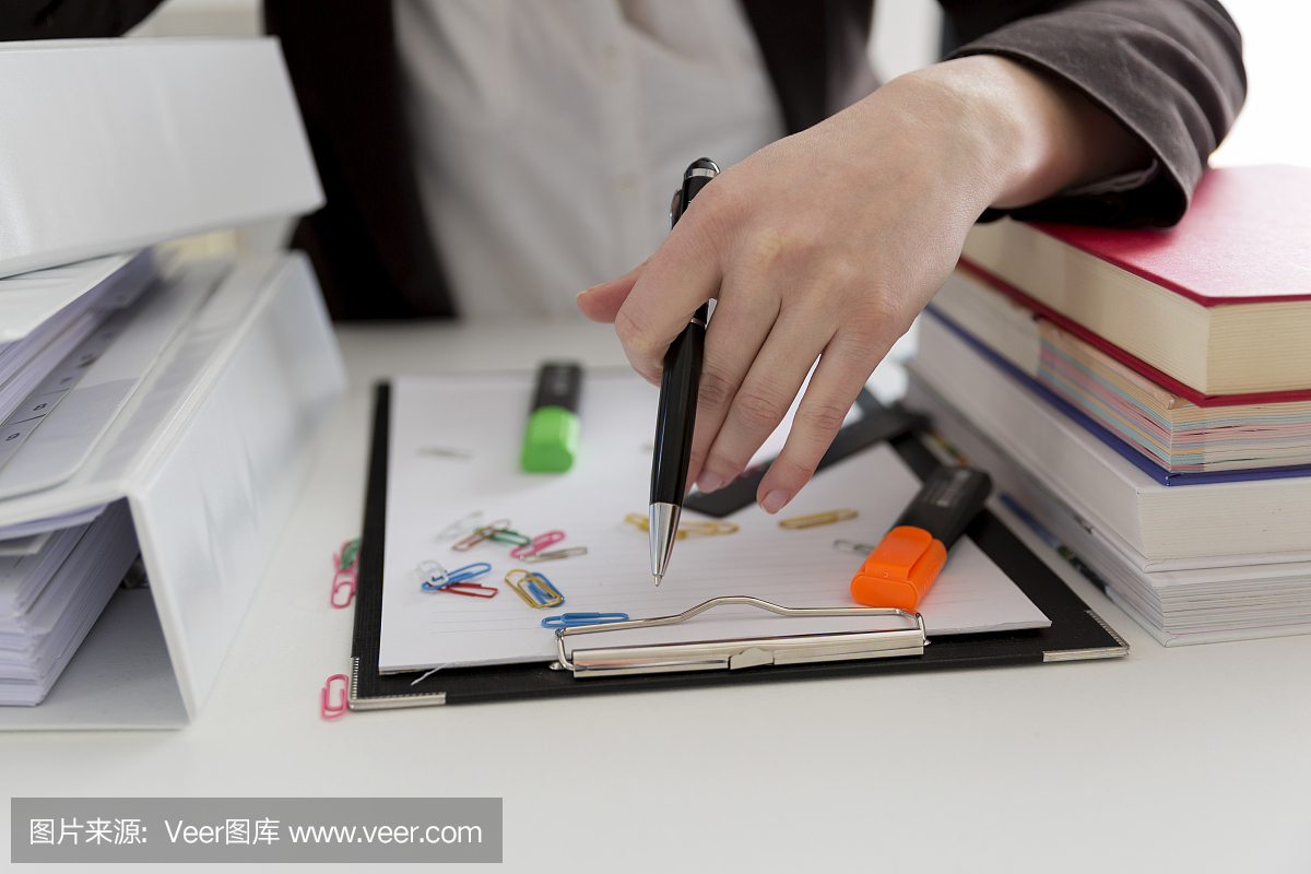 坐在滿是文書,書籍和文件的桌子旁的女人?；靵y的工作場所。過載和過度勞累